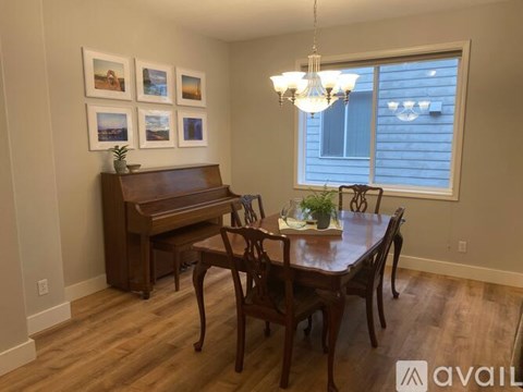 A dining room with a wooden table and chairs, a piano, and pictures on the wall.