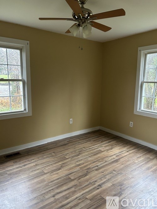 A room with a ceiling fan and two windows.