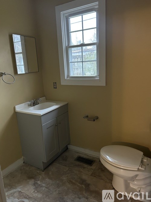 A bathroom with a toilet, sink, and window.