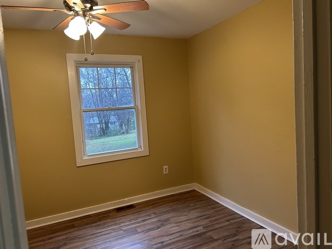 A room with a ceiling fan and a window showing a tree outside.