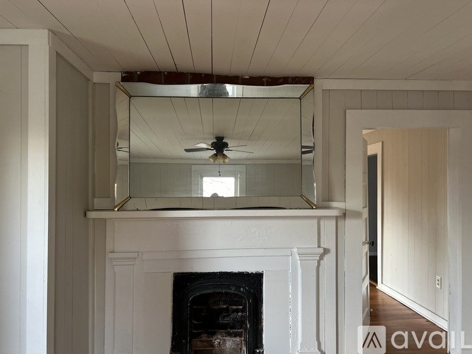 A white fireplace with a mirror above it and a ceiling fan.