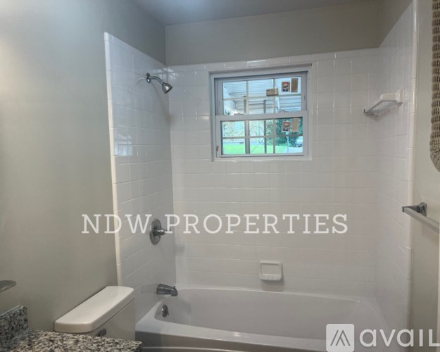 A bathroom with a window and a tub with a shower head.