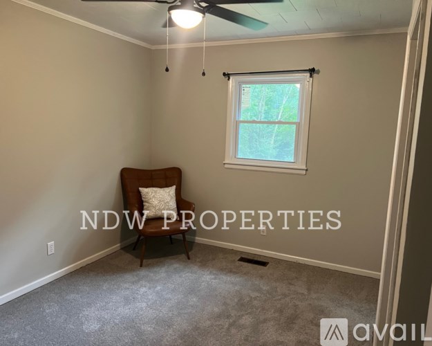 A room with a ceiling fan and a window with a chair in it.