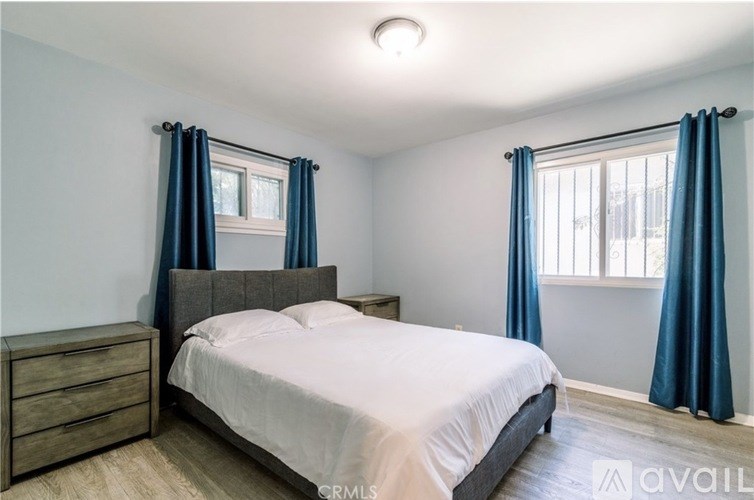 A bedroom with a bed, nightstand, and window with blue curtains.