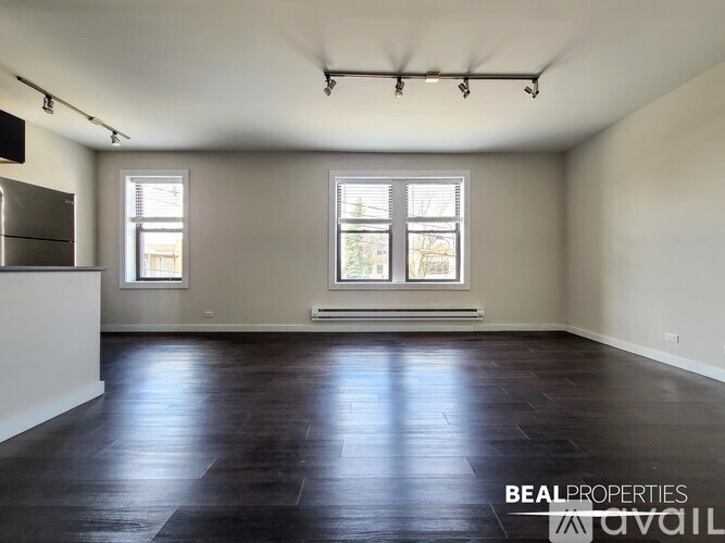 A spacious room with dark wood flooring and two windows.