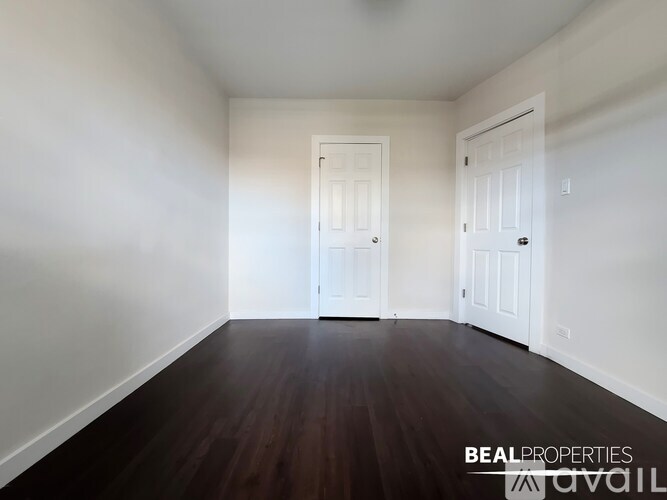 A room with wooden floors and white walls, with two doors and a window.
