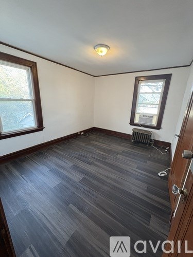 A room with wooden flooring and two windows.