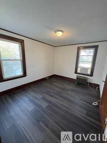 A room with wooden flooring and two windows.