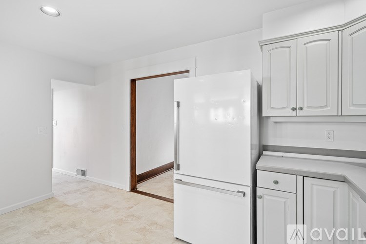 A white refrigerator is in a kitchen with white cabinets.