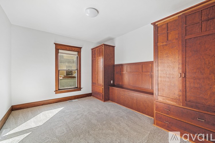 A room with a carpeted floor, wooden furniture, and a window.