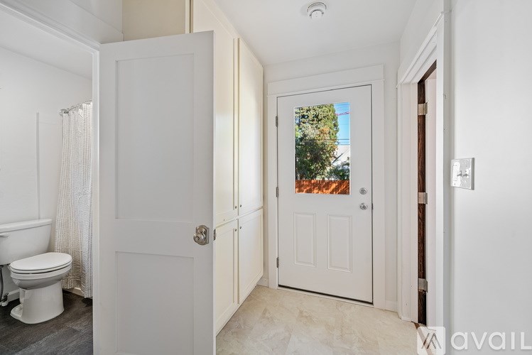 A white bathroom with a toilet, sink, and a door leading to a balcony.