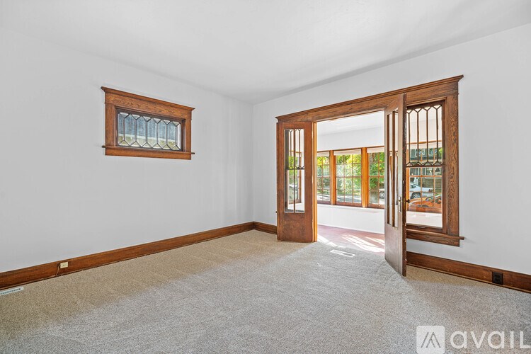 A room with a carpeted floor, a window with a wooden frame, and a door leading to another room.
