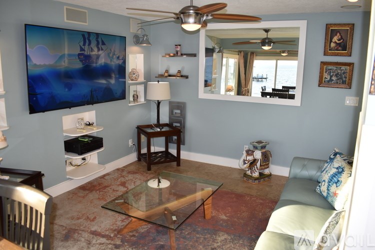 A living room with a glass coffee table and a painting on the wall.