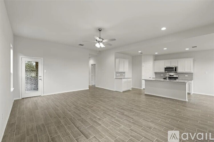 A spacious living room with a ceiling fan and a kitchen area in the background.