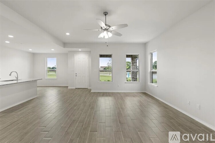 A spacious room with a ceiling fan and light, hardwood flooring, and large windows.