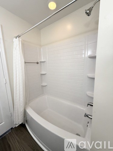 A white bathtub with a shower head and a white curtain.