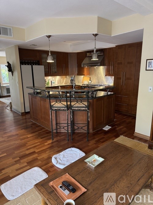 A kitchen with a wooden floor and a center island with a bar stool.