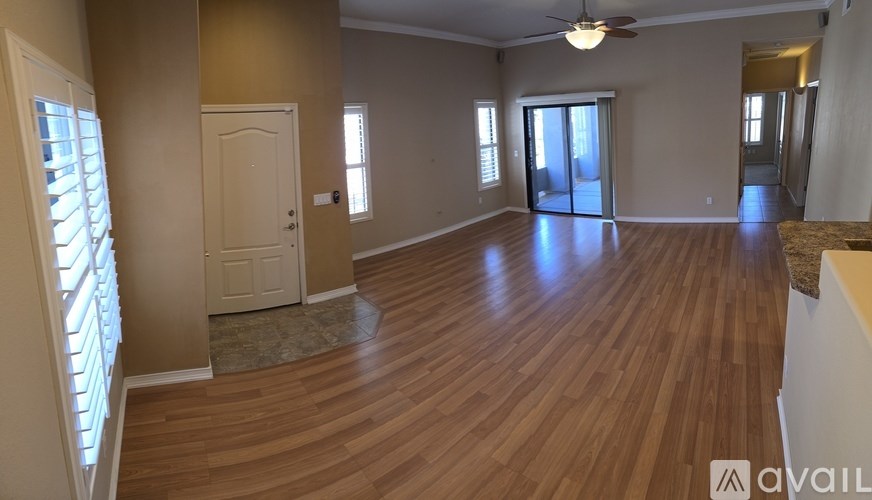 A large empty room with wooden floors and a kitchen in the background.