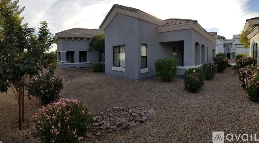 A modern house with a grey exterior is surrounded by a gravel driveway and landscaped with small bushes and flowers.