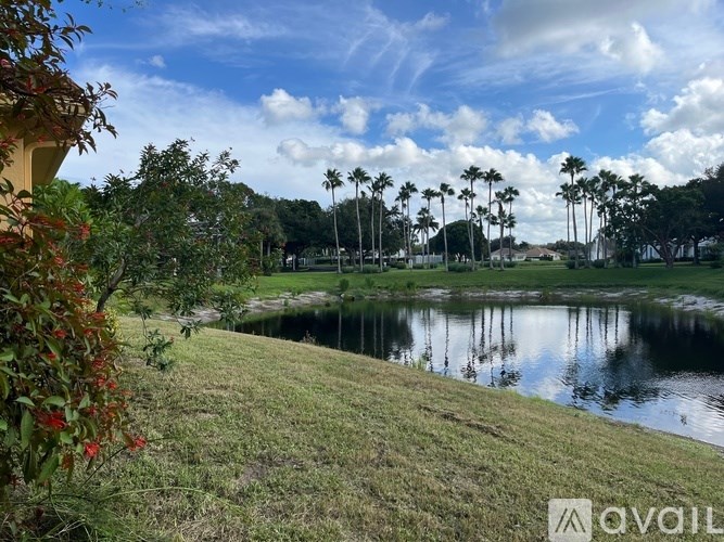 A serene landscape with a pond, palm trees, and a partly cloudy sky.