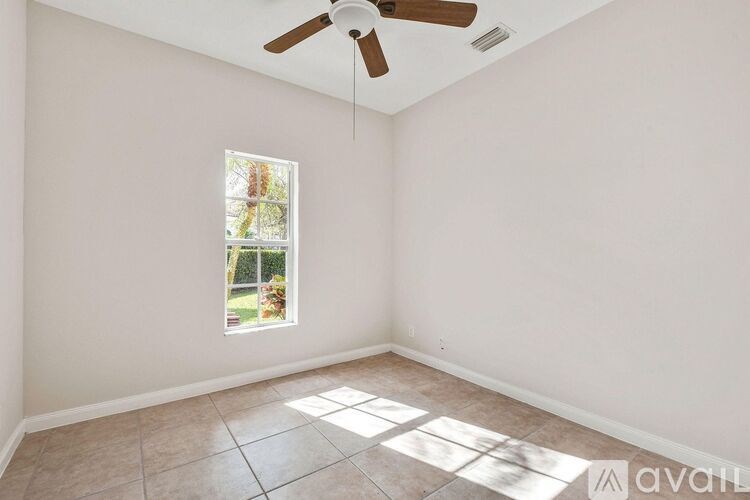 A room with a ceiling fan and a window showing a garden outside.