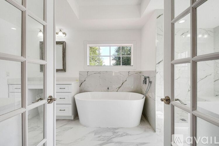 A white bathroom with a marble floor and a large tub.