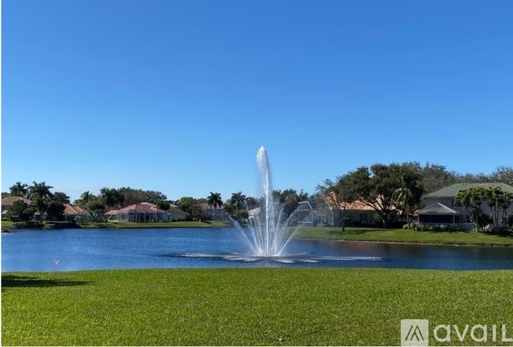 A fountain in the middle of a grassy area with houses in the background.