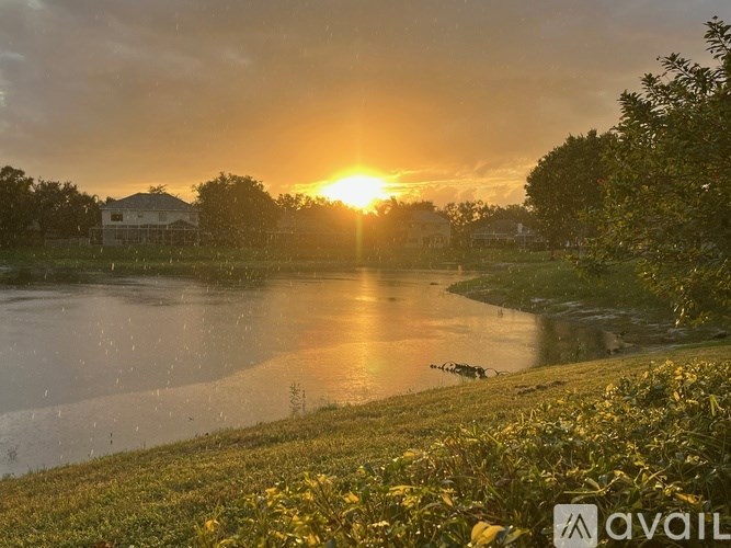 A sunset over a lake with a house and trees in the background.
