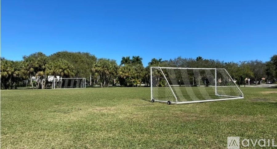 A soccer goal stands on a grassy field with trees in the background.