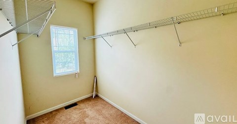 A room with a carpeted floor, a window with blinds, and a metal rack on the wall.