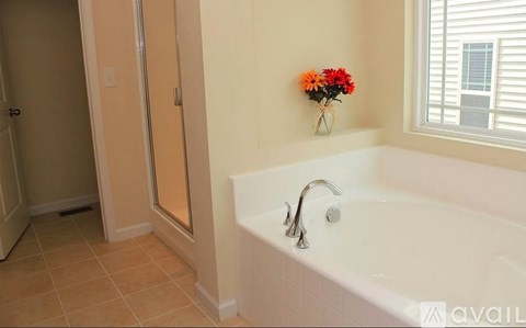 A white bathtub with a silver faucet and a vase of flowers on the wall.