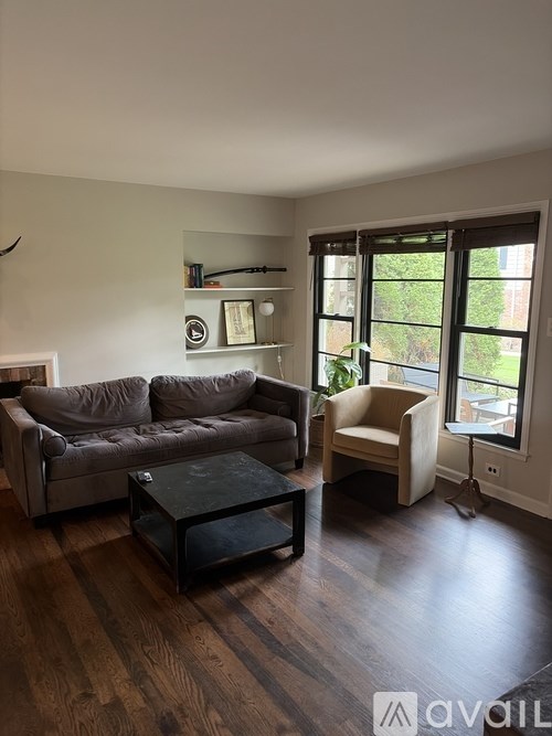 A living room with a grey couch, a black coffee table, and a window with a view of greenery outside.