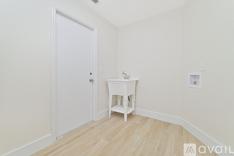 A white door is on the left of a room with a small white table and a framed picture on the wall.