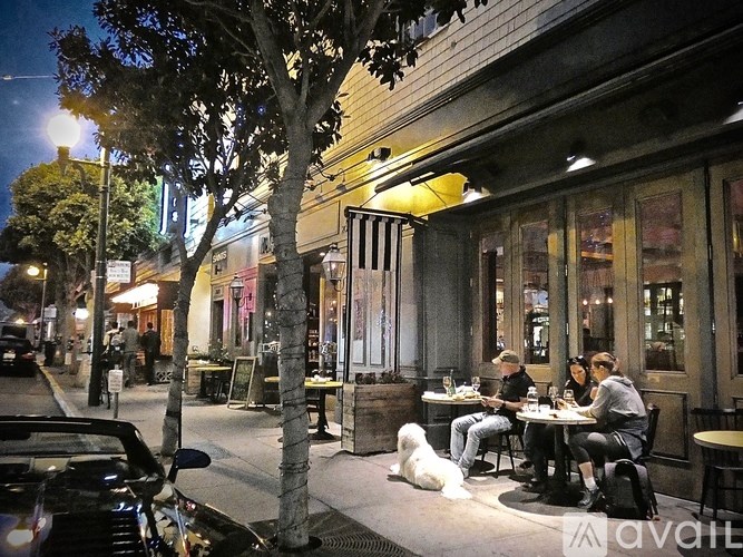 A group of people are sitting at a table outside a restaurant with a dog sitting in front of them.
