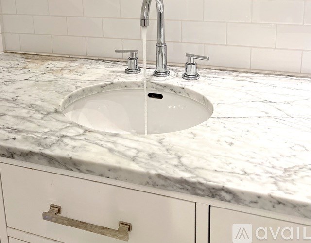 A white sink with a silver faucet is in the middle of a marble countertop.