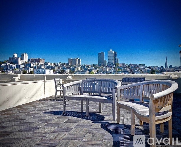 A wooden chair and bench are on a rooftop terrace with a city skyline in the background.