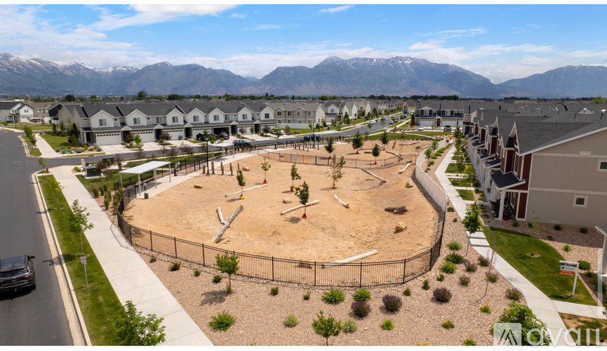 A playground with a fence and a dirt area in the middle of a residential area with houses and cars.