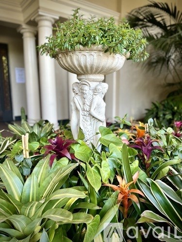 A white planter with a statue on top is surrounded by green plants.