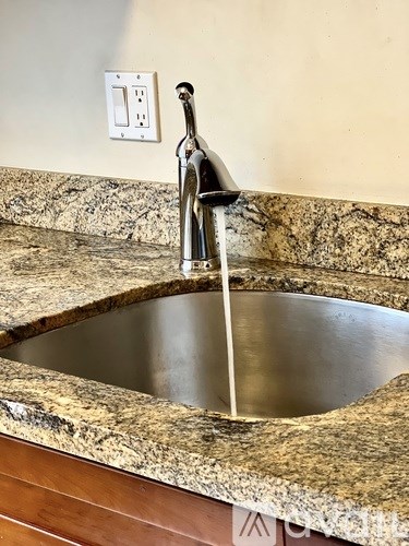 A sink with a running tap and a marble countertop.