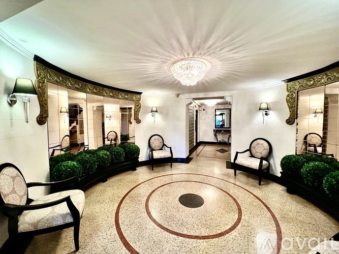 A well-lit, elegant hallway with a circular design on the floor and a chandelier hanging from the ceiling.