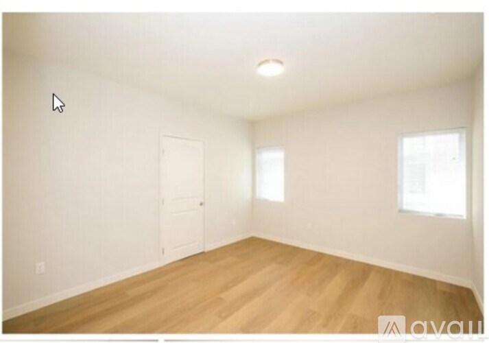 A room with wooden floors and white walls, with a door and a window.