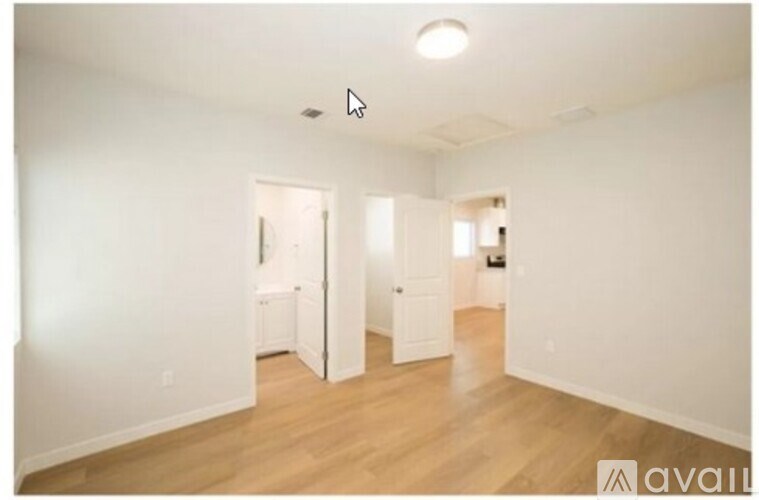 A room with white walls and wooden flooring, with a door on the left and a window on the right.