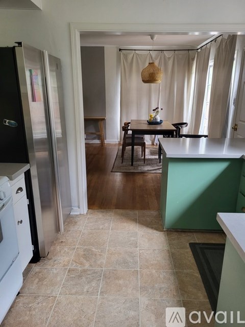 A kitchen with a black fridge and stainless steel dishwasher next to a dining table with a hanging light.