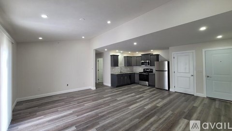 A spacious room with wooden flooring and a kitchen area in the background.
