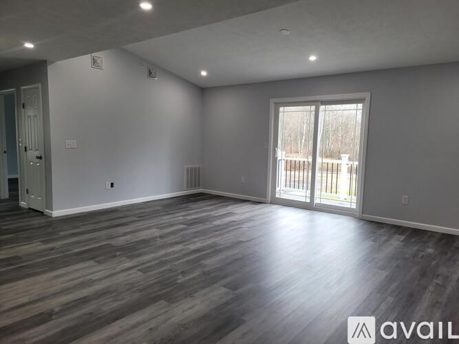 A spacious room with wooden flooring and a sliding glass door.