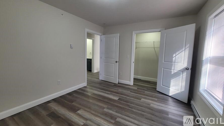 A room with white walls and wooden flooring, with two doors open.