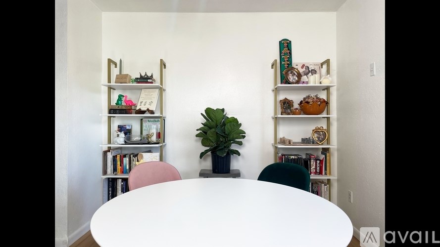 A white table is in the middle of a room with two shelves on the wall.