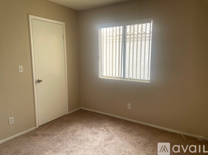 A room with a carpeted floor, a door, and a window with blinds.