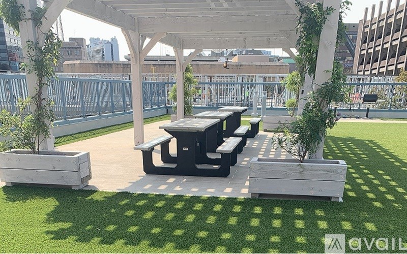 A white pergola is over a table and benches in a grassy area.