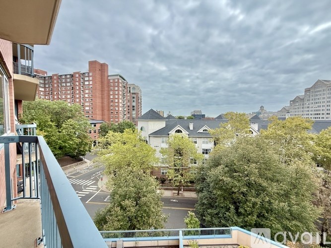 A view from a balcony overlooking a city street with buildings and trees.